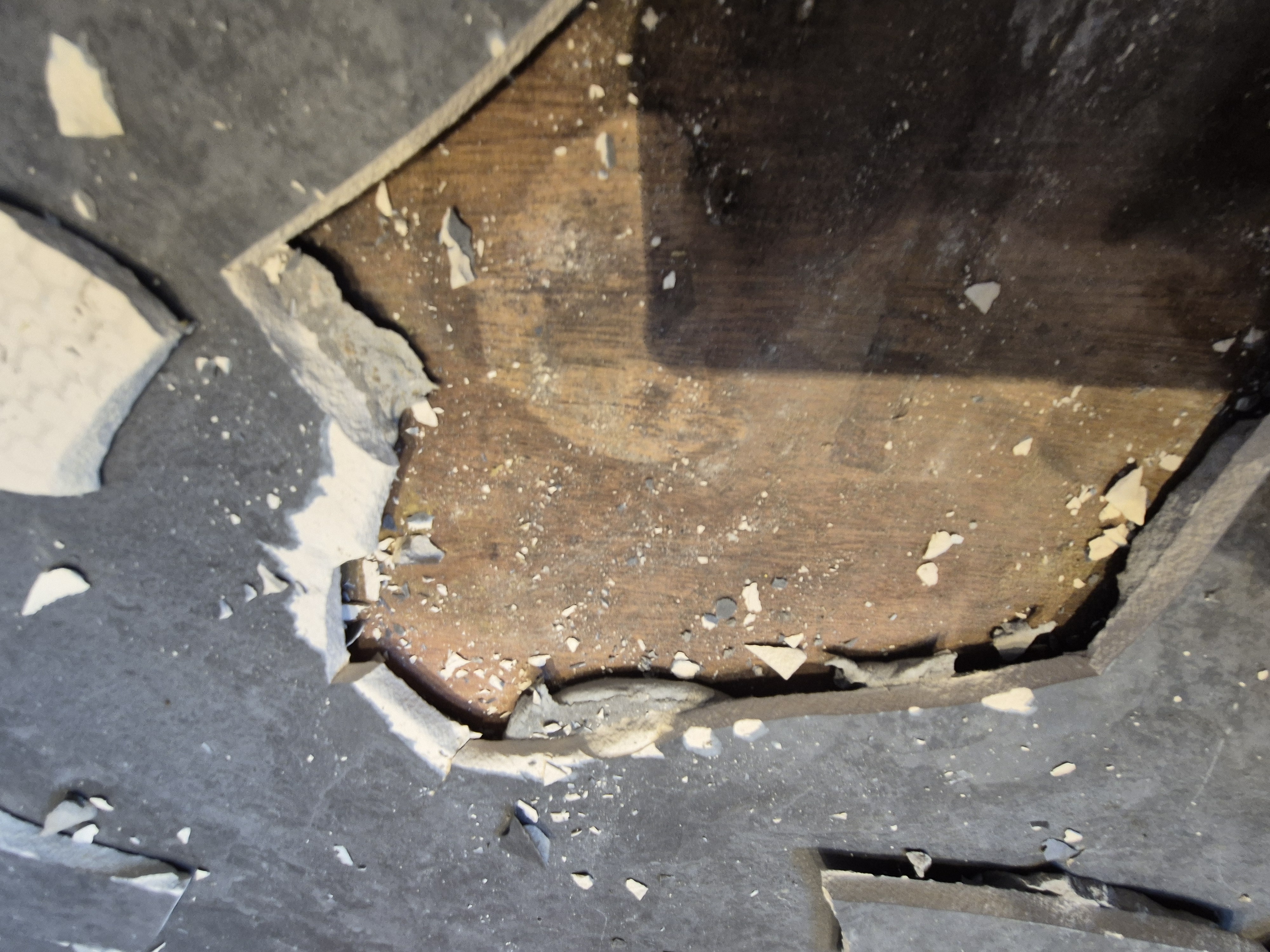Grey slate floor tiles being lifted to expose the plywood beneath